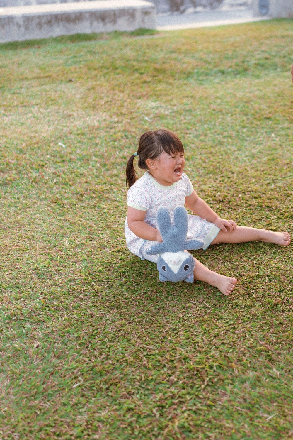 Small child in white dress sitting and playing on green grass outdoors.