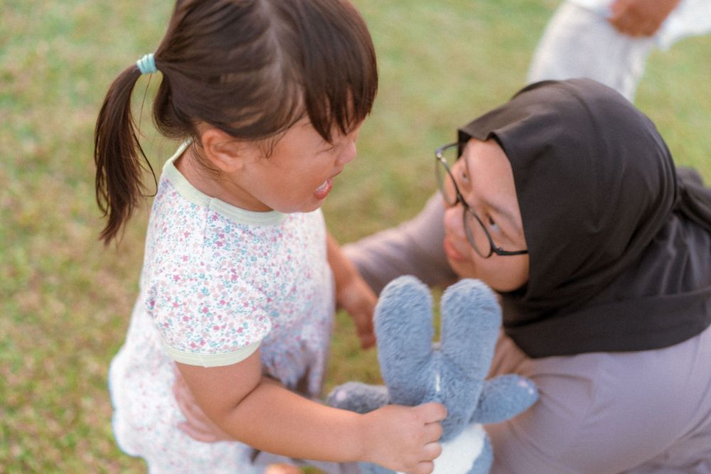 A tender moment shared between parent and child playing with a blue stuffed toy outdoors.
