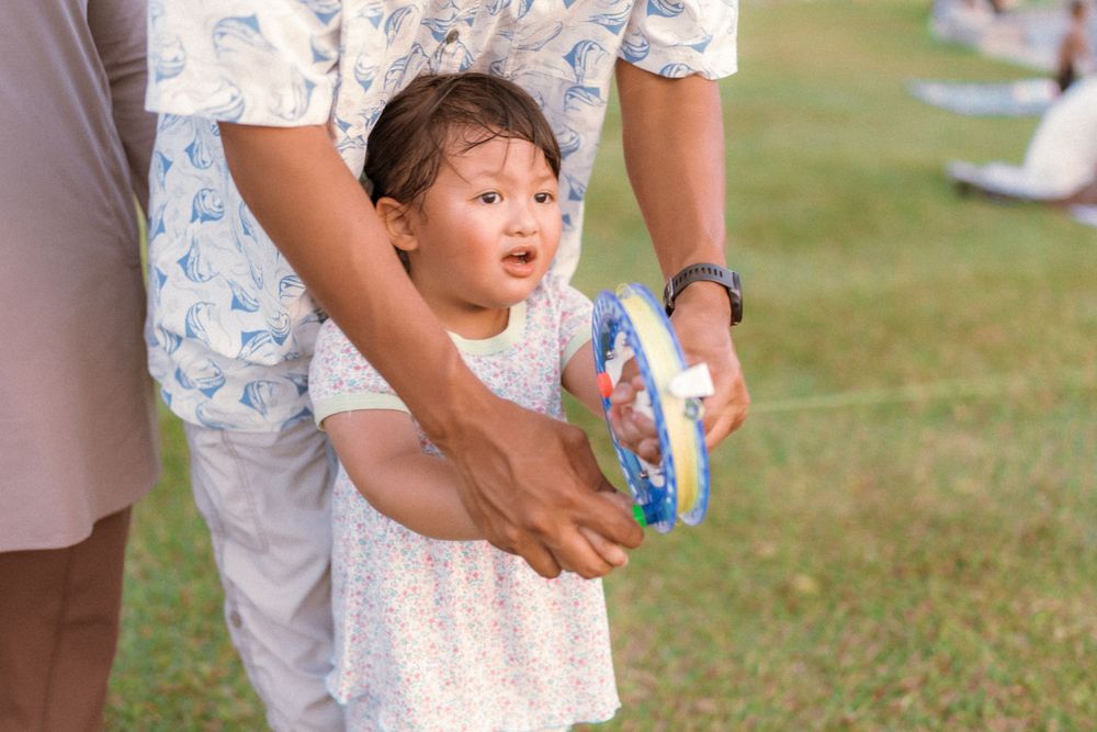 A child plays with a bubble toy while being helped by someone in light clothing.