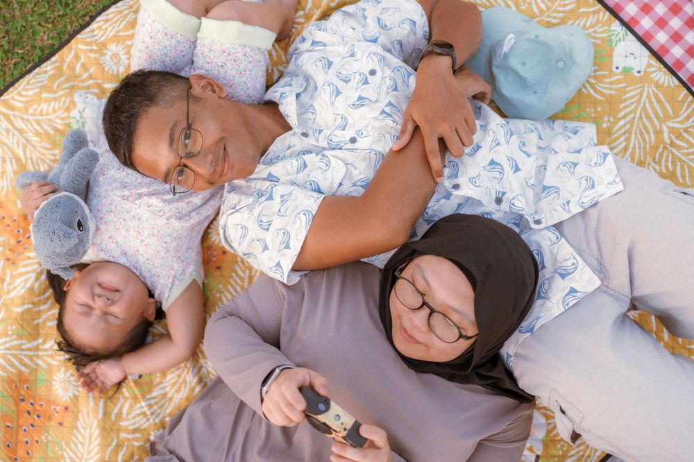 A happy family relaxes together on a patterned blanket with stuffed toys during an outdoor picnic.