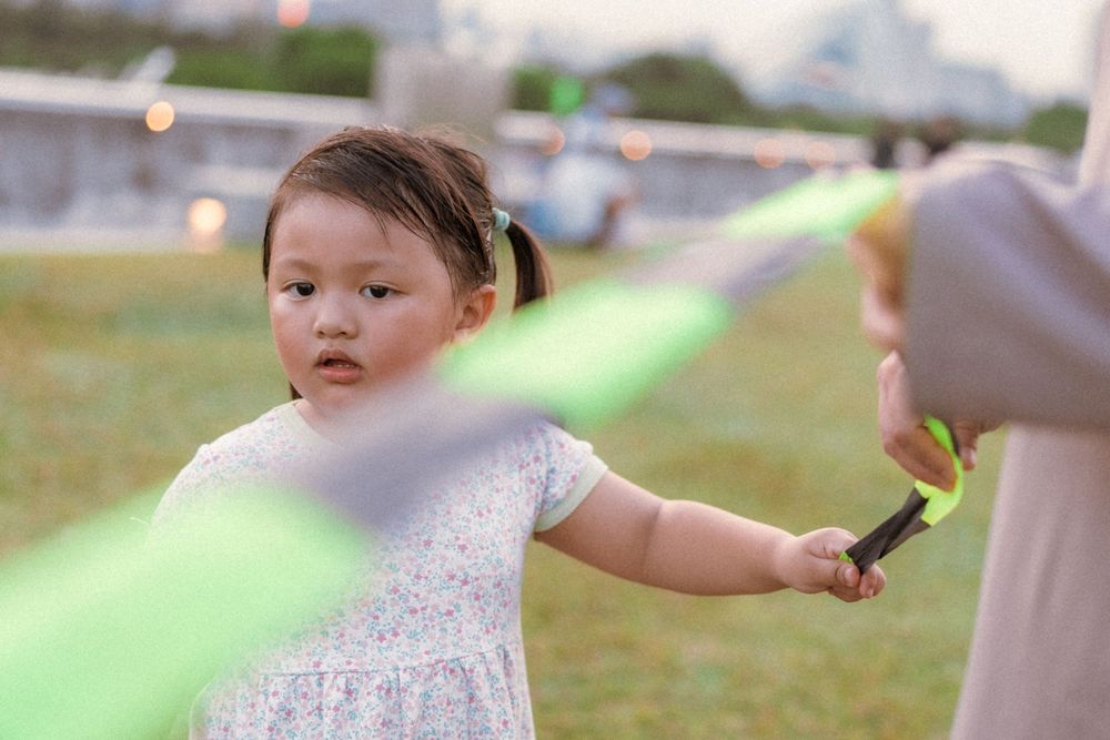 A child in a white dress plays with a light-up toy at dusk in a park.