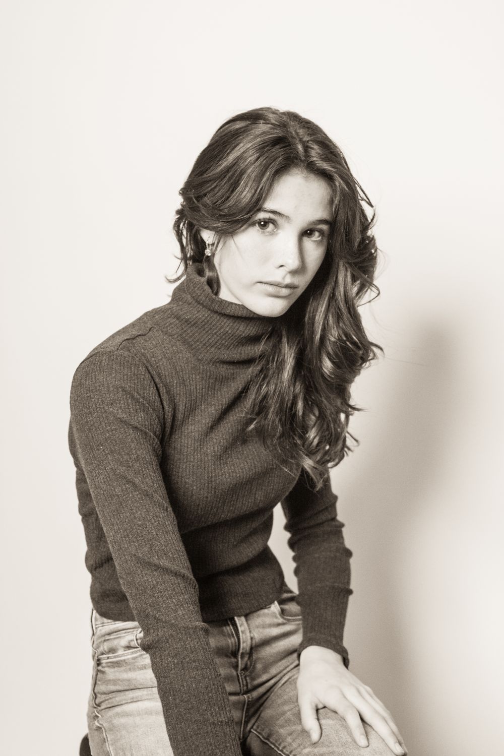 Studio portrait of woman in turtleneck sweater and jeans with styled dark hair.