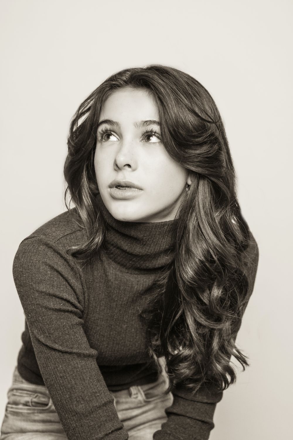 Artistic portrait of woman in brown turtleneck looking up with styled waves.