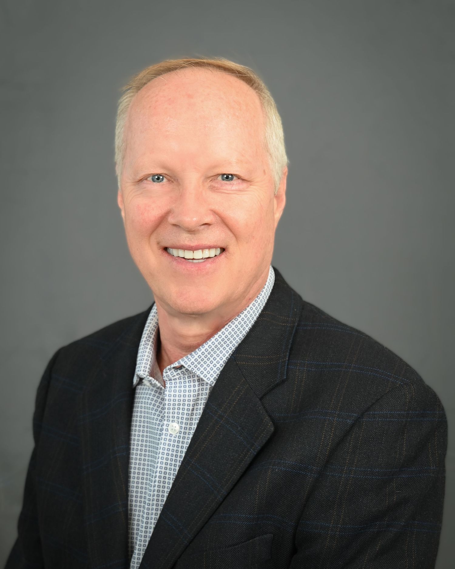 Professional headshot against grey background wearing business attire.