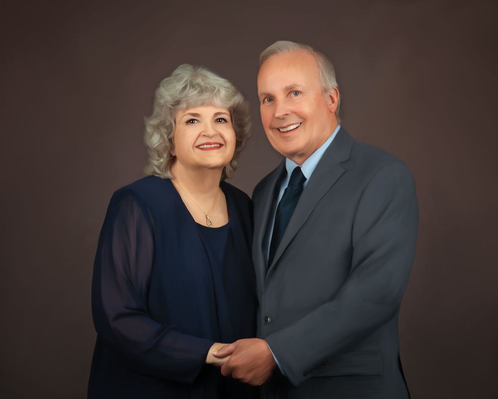 A couple poses together for a formal portrait wearing navy blue and gray against a dark brown backdrop.