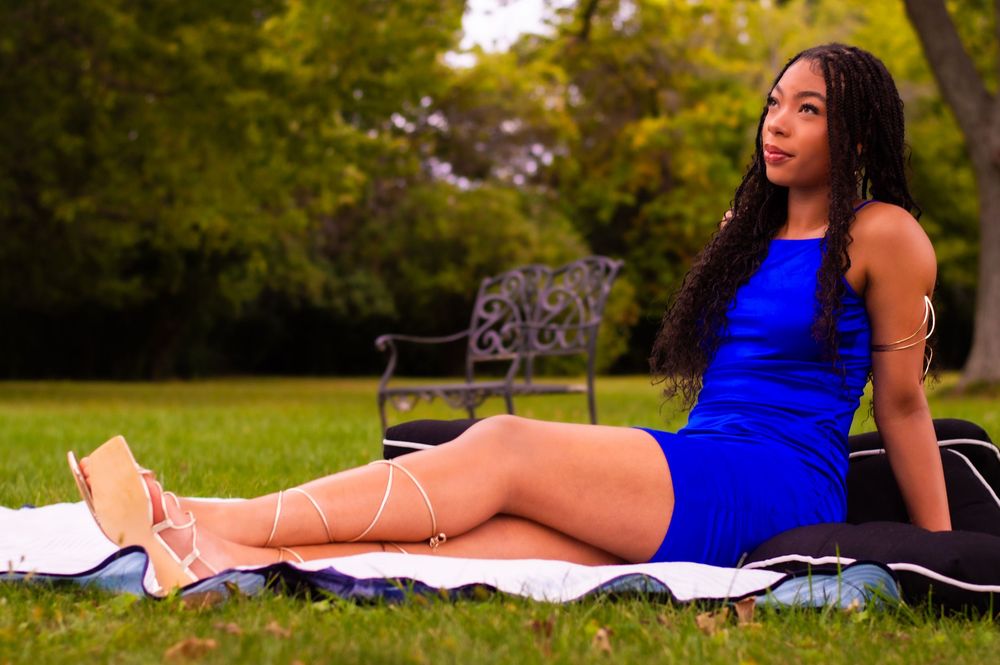 Person in royal blue dress relaxing on picnic blanket in sunny park setting.