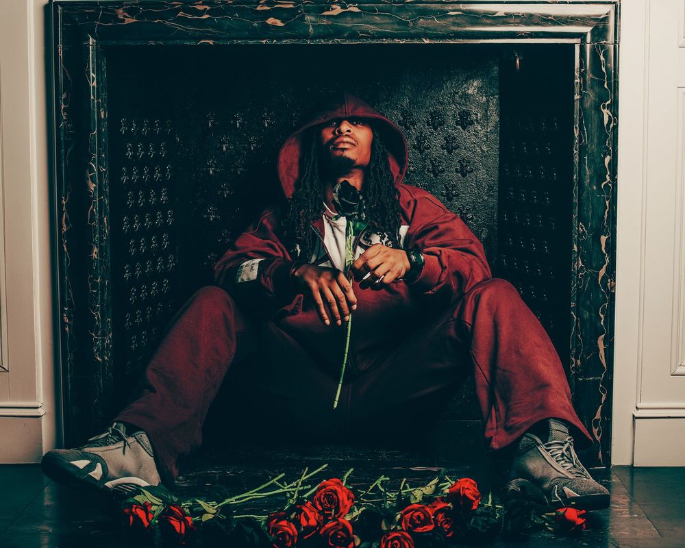 Person in red outfit sitting among roses in dark setting.