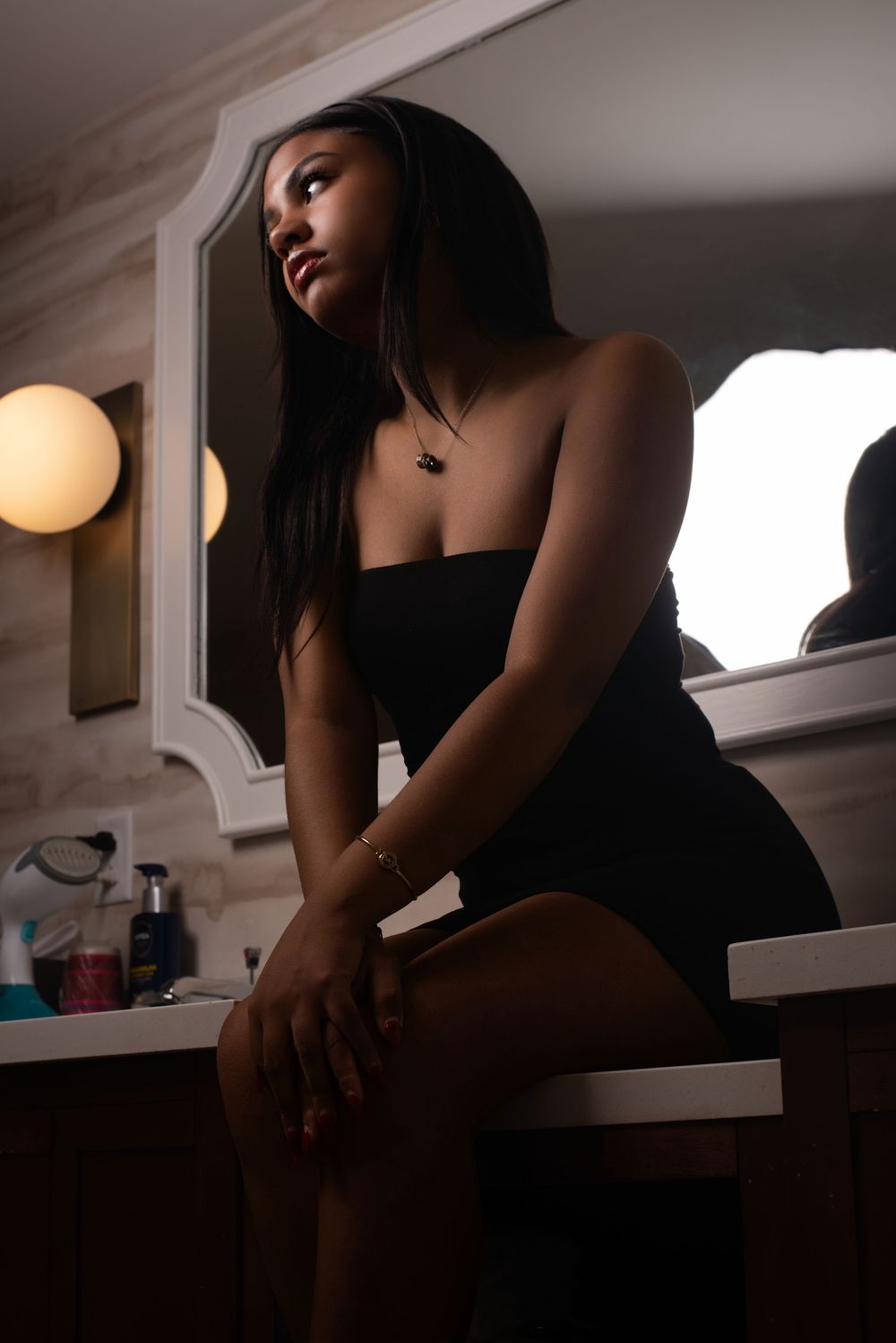 Moody portrait in dark bathroom with warm lighting and minimalist aesthetic.