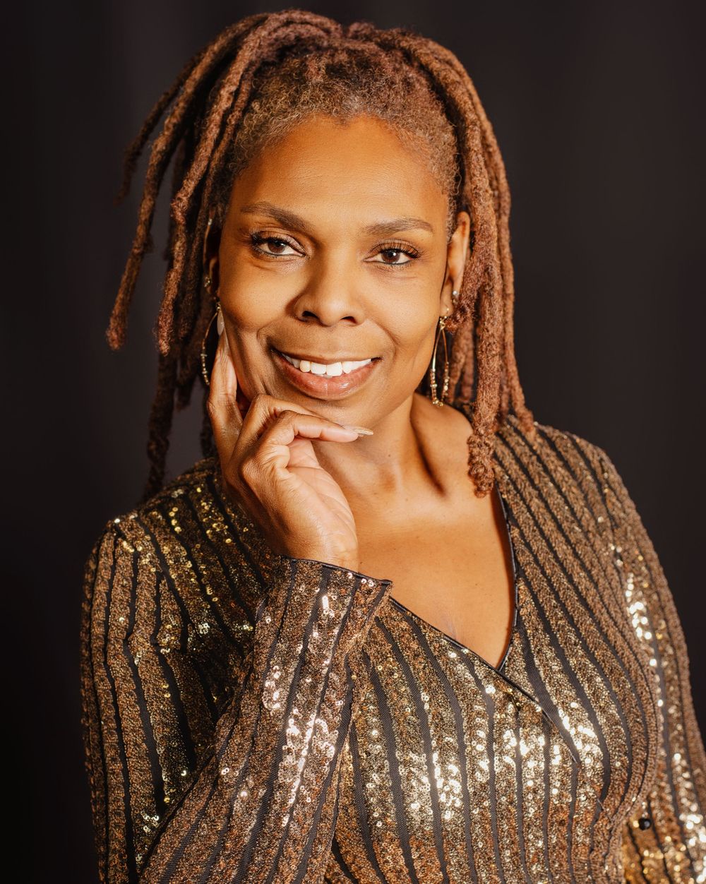 Portrait featuring sparkly gold dress and styled locs against dark background.