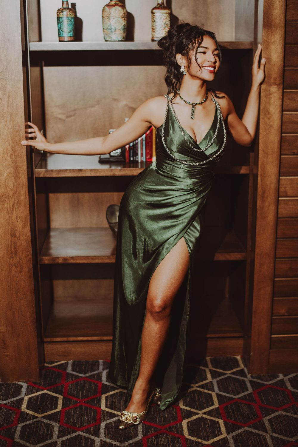 Model in emerald silk dress poses elegantly against rustic wooden shelving.