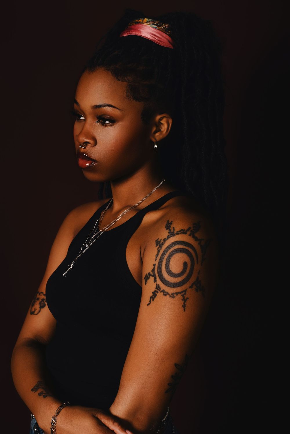Dramatic portrait showing circular tattoo art and red visor against dark background.