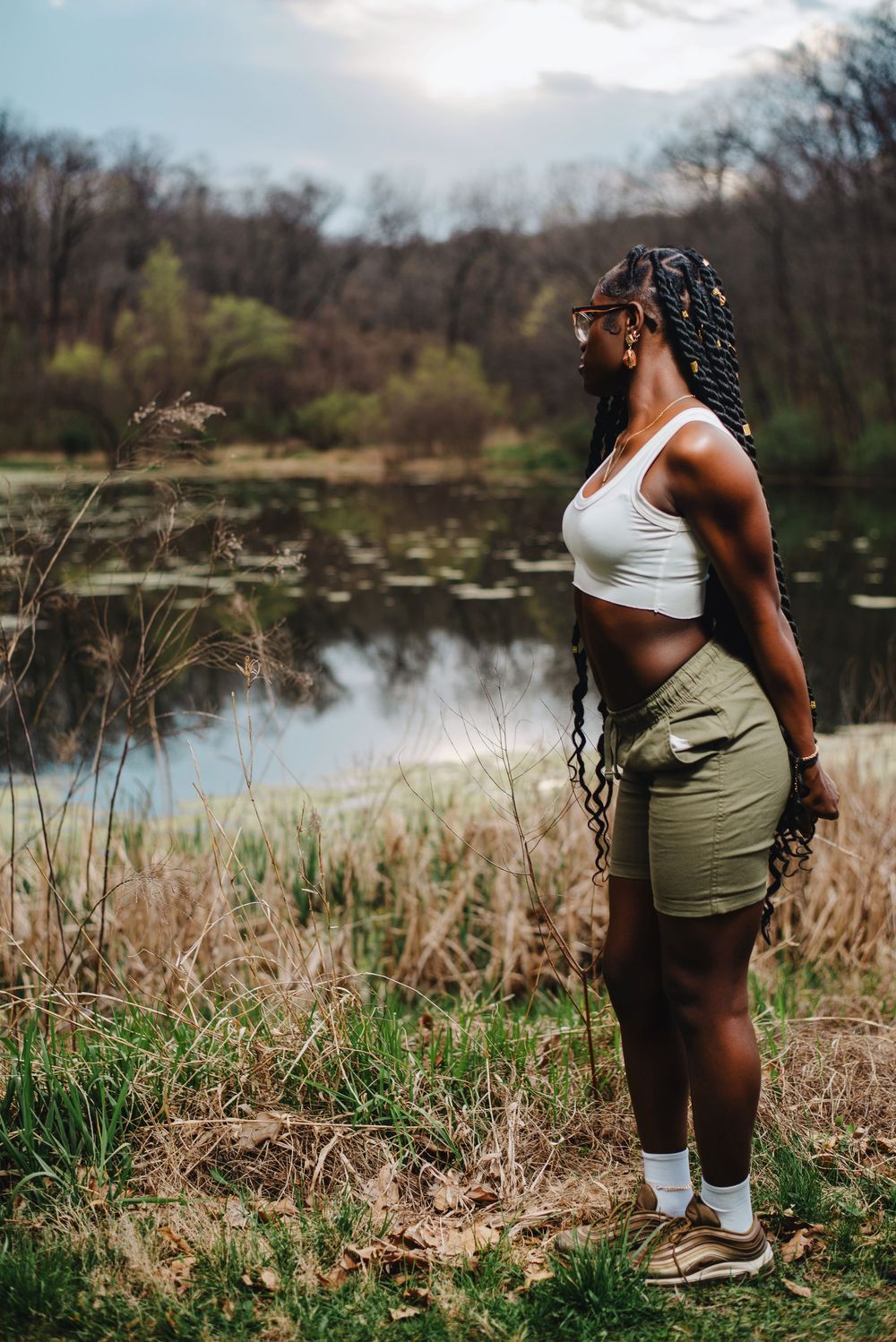 Athletic figure in workout attire standing by serene pond landscape.