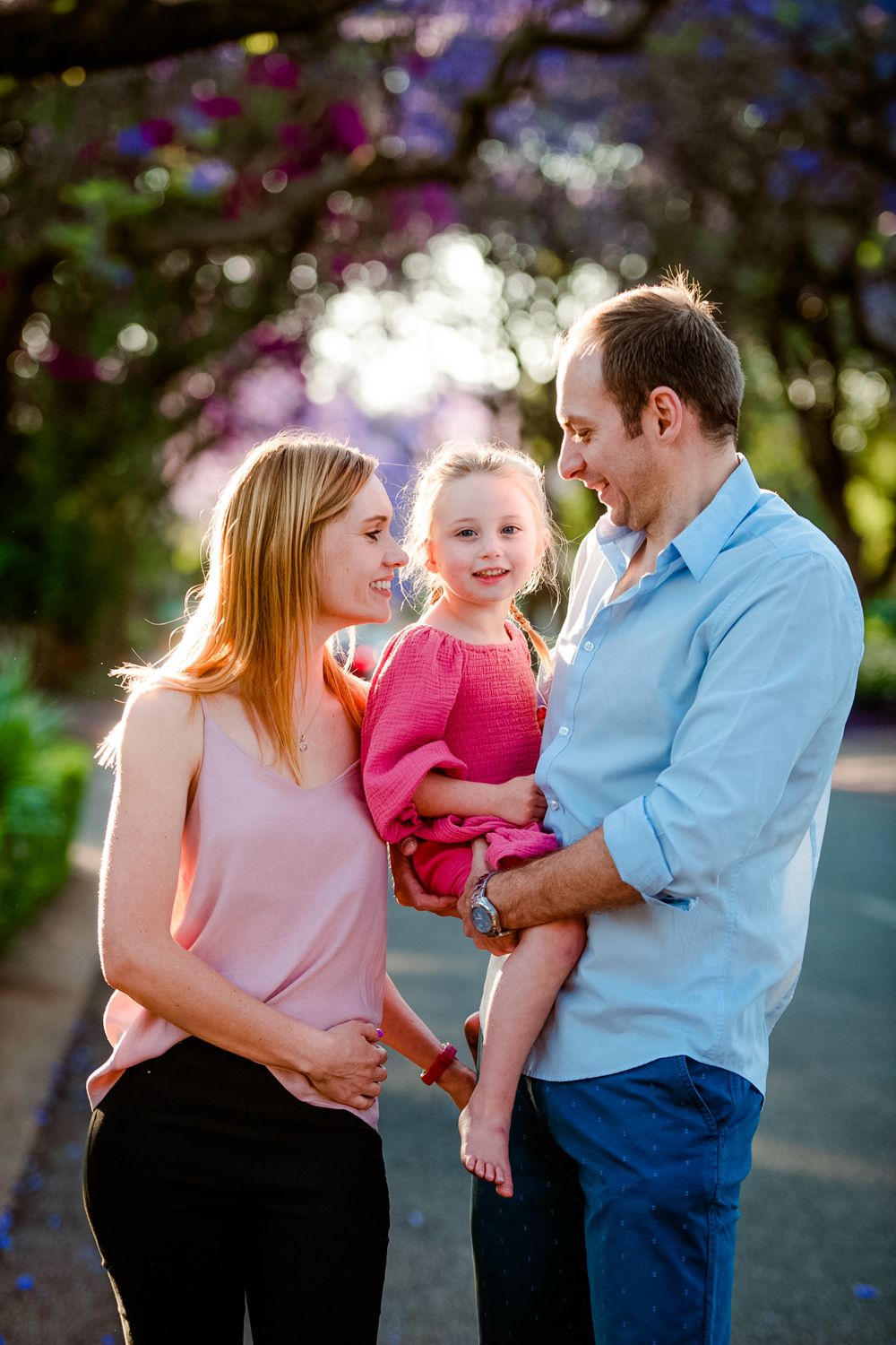 Family of three posing under the purple Jacaranda trees during a photoshoot in Pretoria.