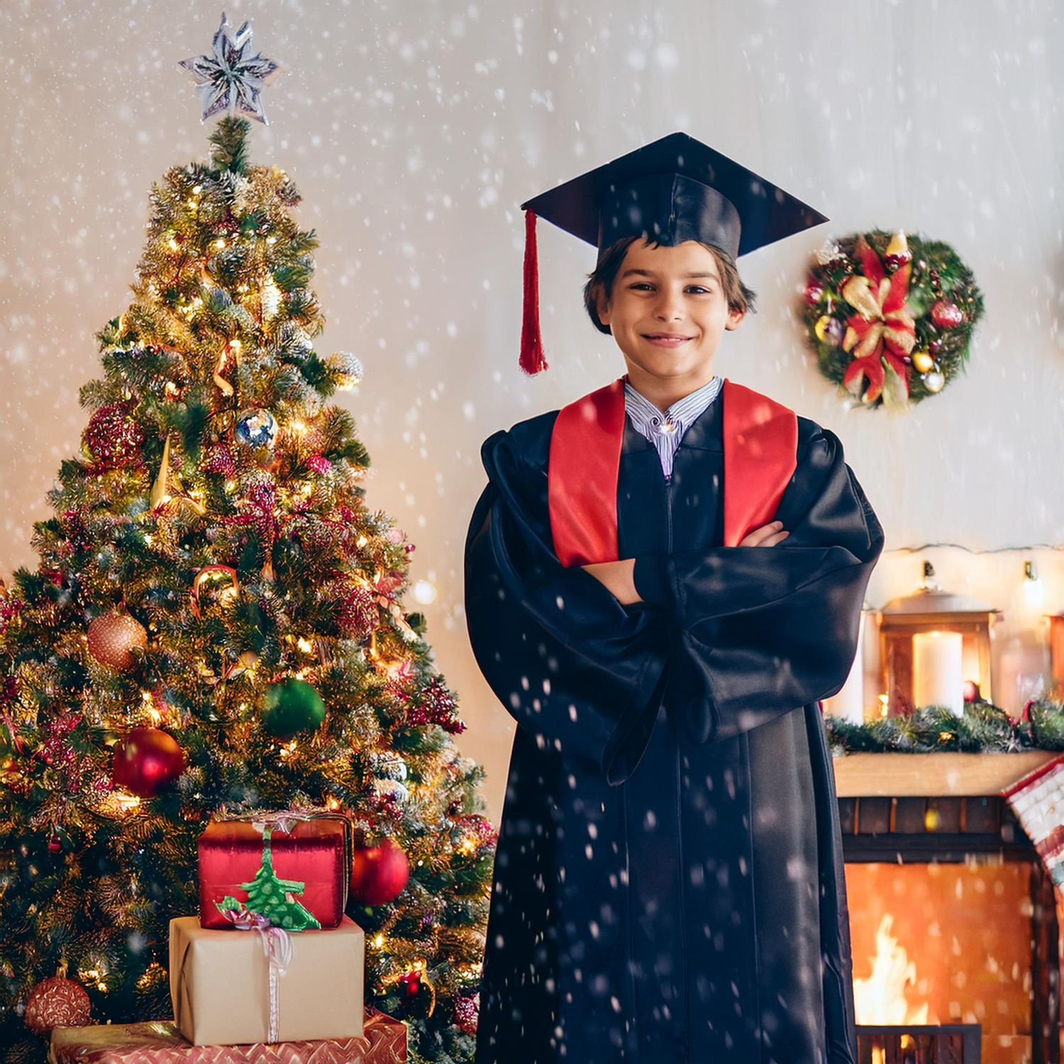 A graduate in cap and gown poses by a decorated Christmas tree with wrapped presents.