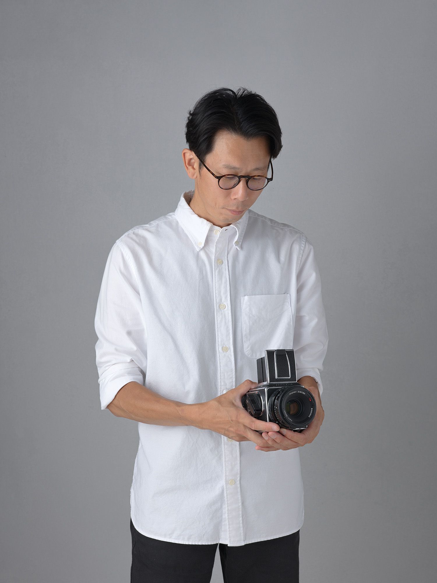 Black and white studio portrait of a person in glasses and dark sweater against simple background. Photographer Noritoshi Ichikawa. Toronto