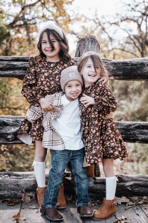 Two children sitting on rustic wooden deck wearing coordinated fall outfits with boots during autumn photo session.