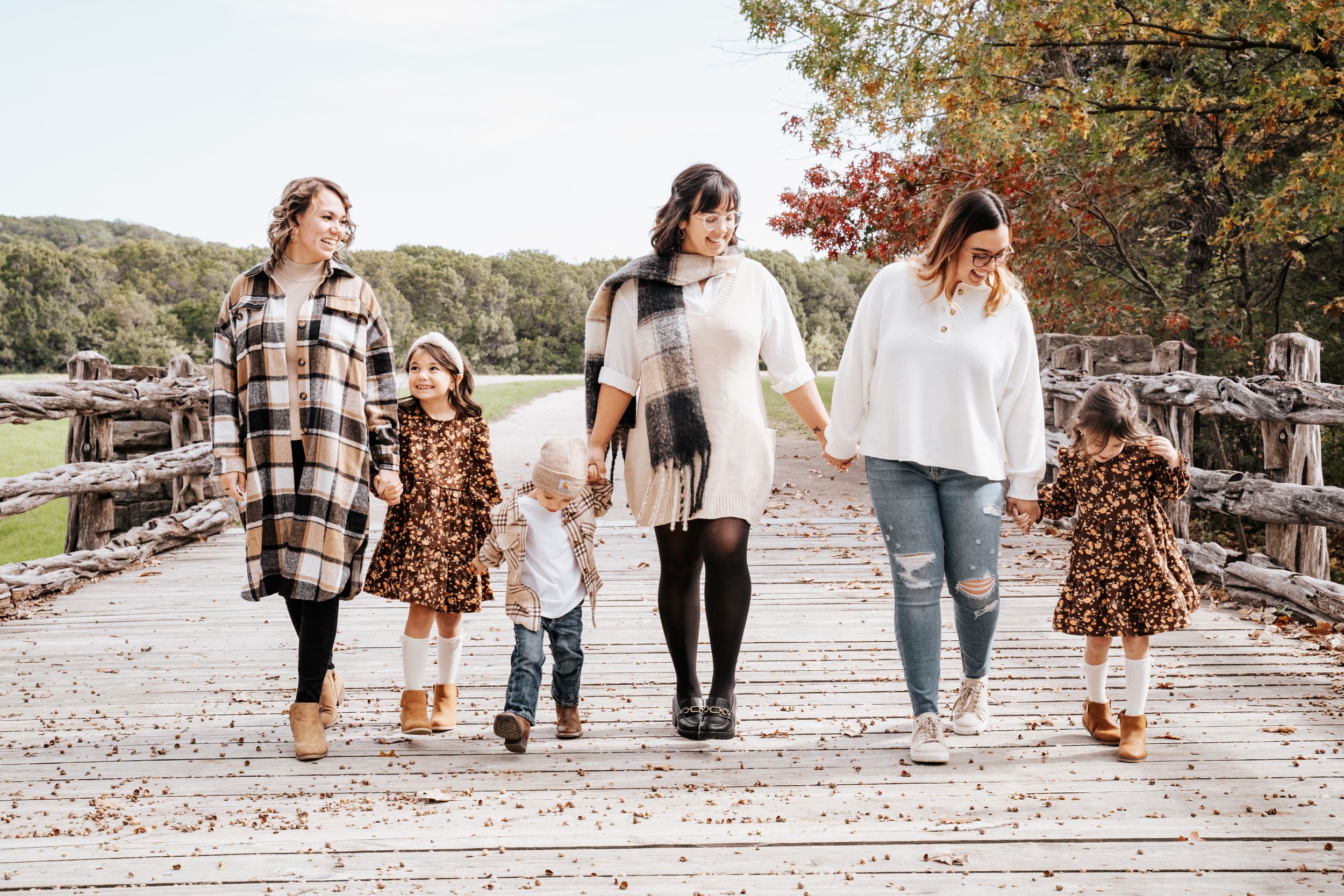 Family walking together on wooden bridge path during autumn outdoor photography session.