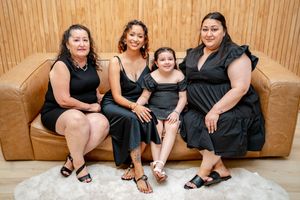 Group portrait of people in black attire sitting together on a tan leather couch.