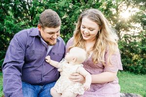 Parents sharing sweet moments with baby in lush green outdoor setting.
