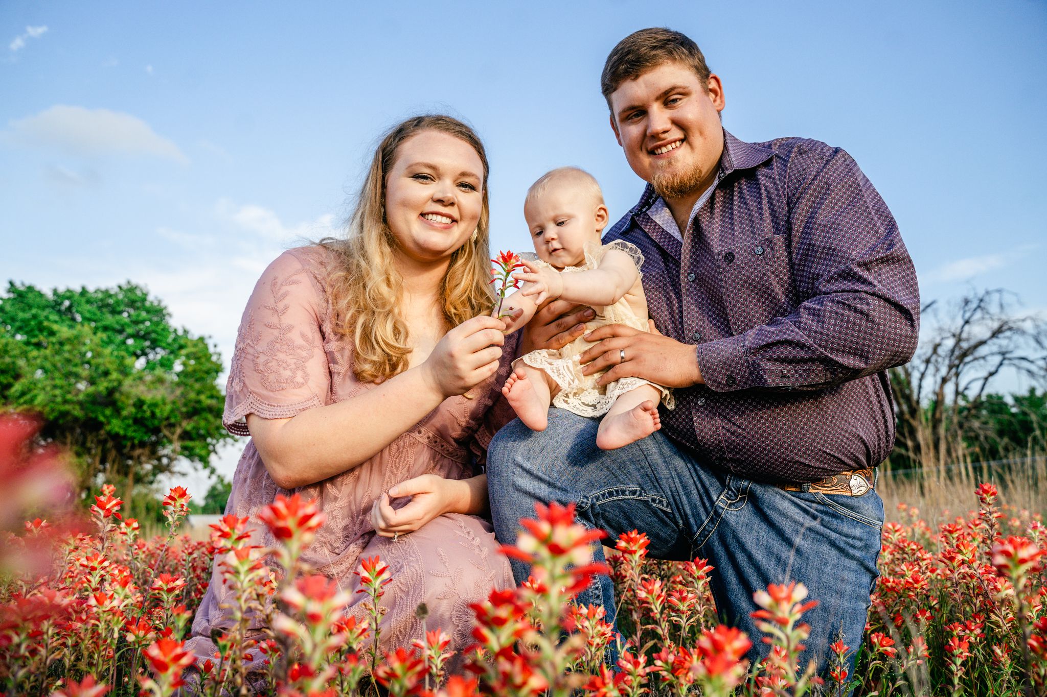Family portrait in vibrant red wildflower field under blue sky.