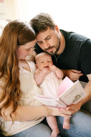 Family reads a storybook together while cuddling on a couch.