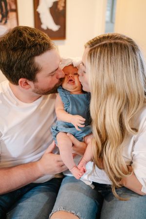 Parents cuddle and play with their baby in casual home setting.
