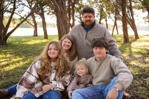 Family group portrait taken outdoors under tall pine trees in casual attire.
