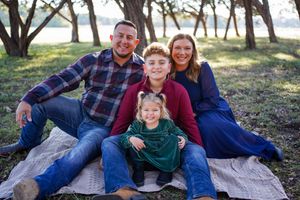 Family relaxing together on blanket during casual outdoor photo session in wooded setting.