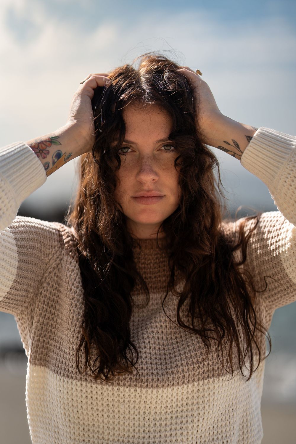 A sequence of four photos showing a person with long dark wavy hair wearing a cream knit sweater against a bright sky.