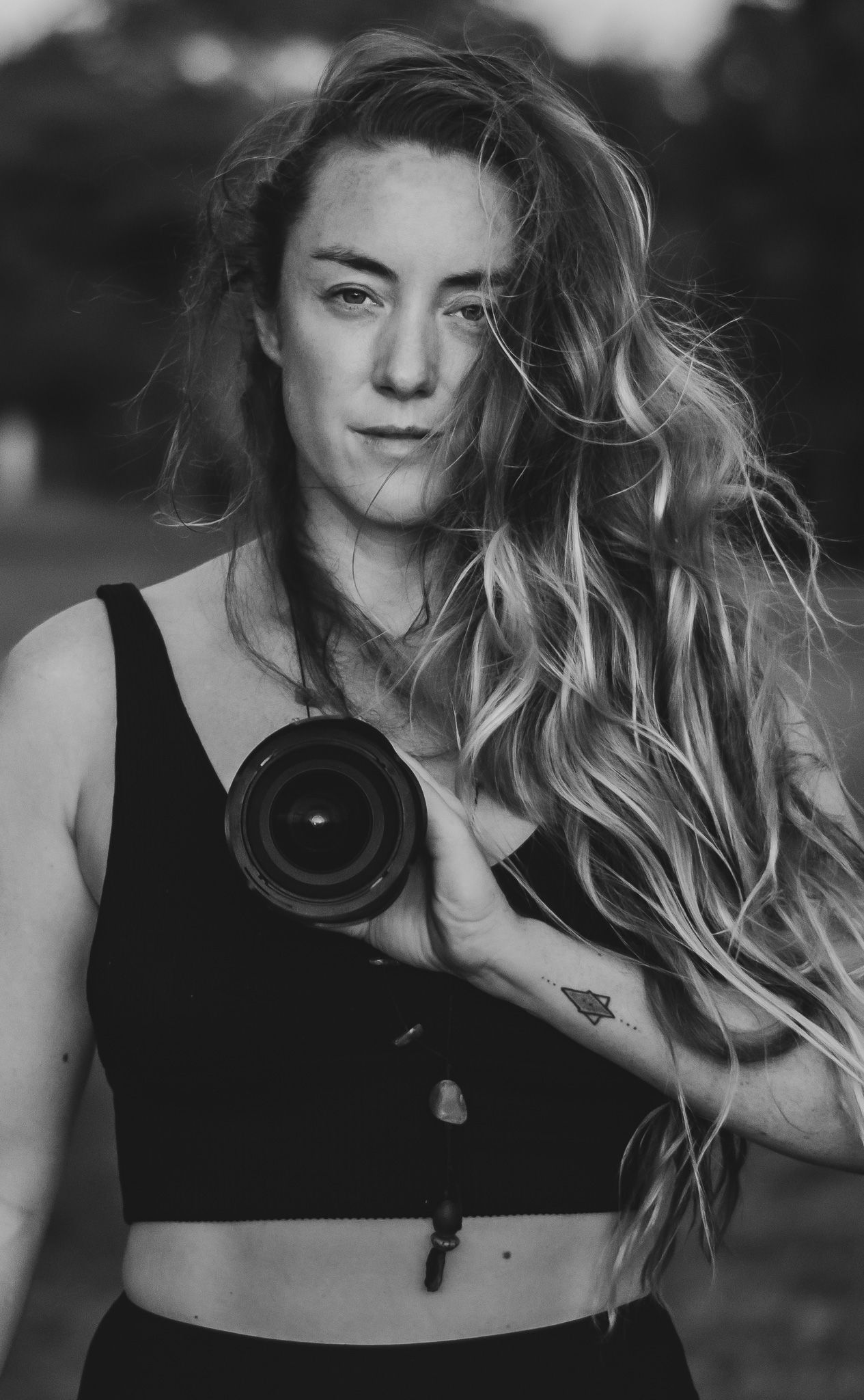Black and white portrait of photographer holding professional camera with long flowing hair.