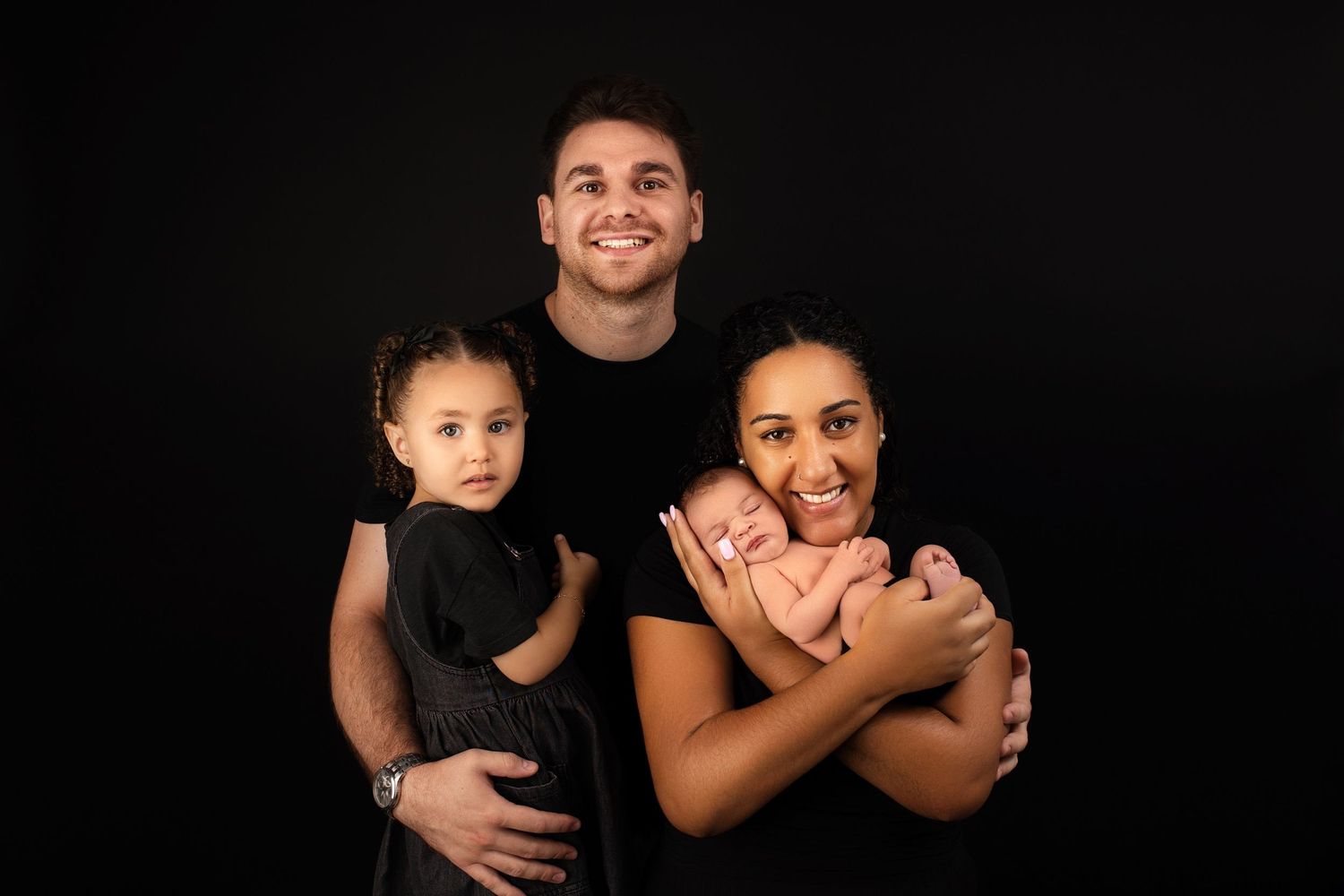 Portrait of a family of three against black background.