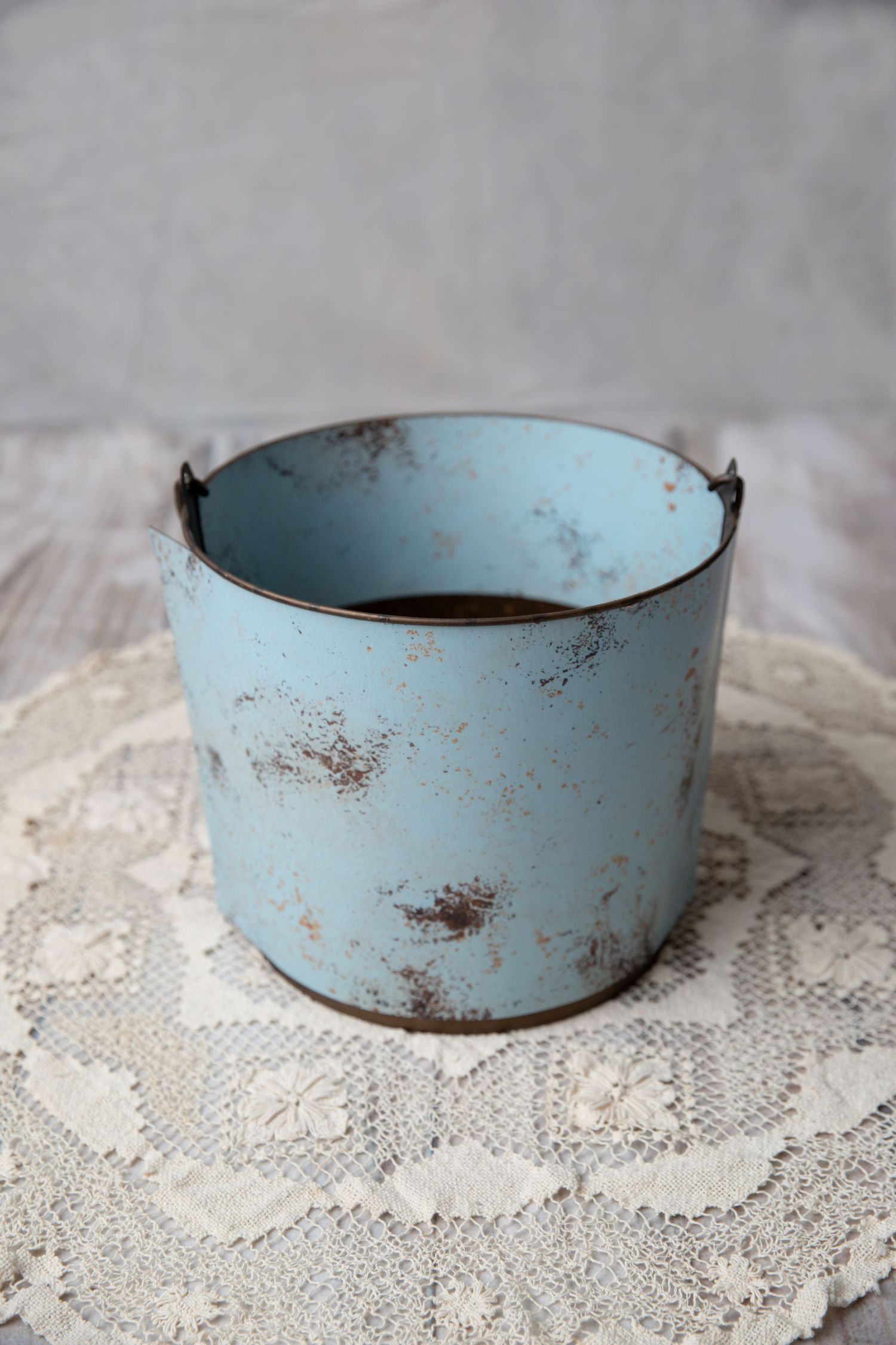 Antique distressed pale blue metal pail with worn paint on a white lace doily.