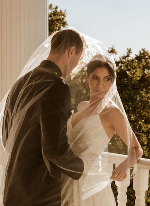 Sepia-toned wedding photo on classic white columned porch with flowing veil.