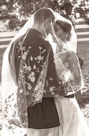 Black and white portrait of couple sharing tender moment under floral veil.
