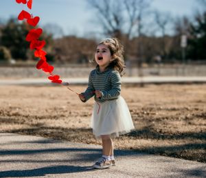 Child in tulle skirt laughing with red heart decorations floating above.