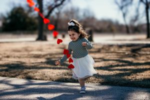 Young child running along path with floating red hearts in winter scene.