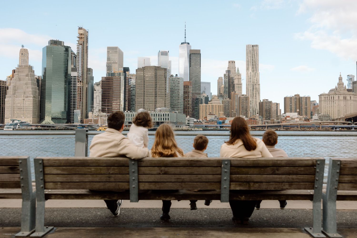 A family gazes over the Hudson River toward the New York City skyline, capturing a quiet, reflective moment with a sweeping urban backdrop.