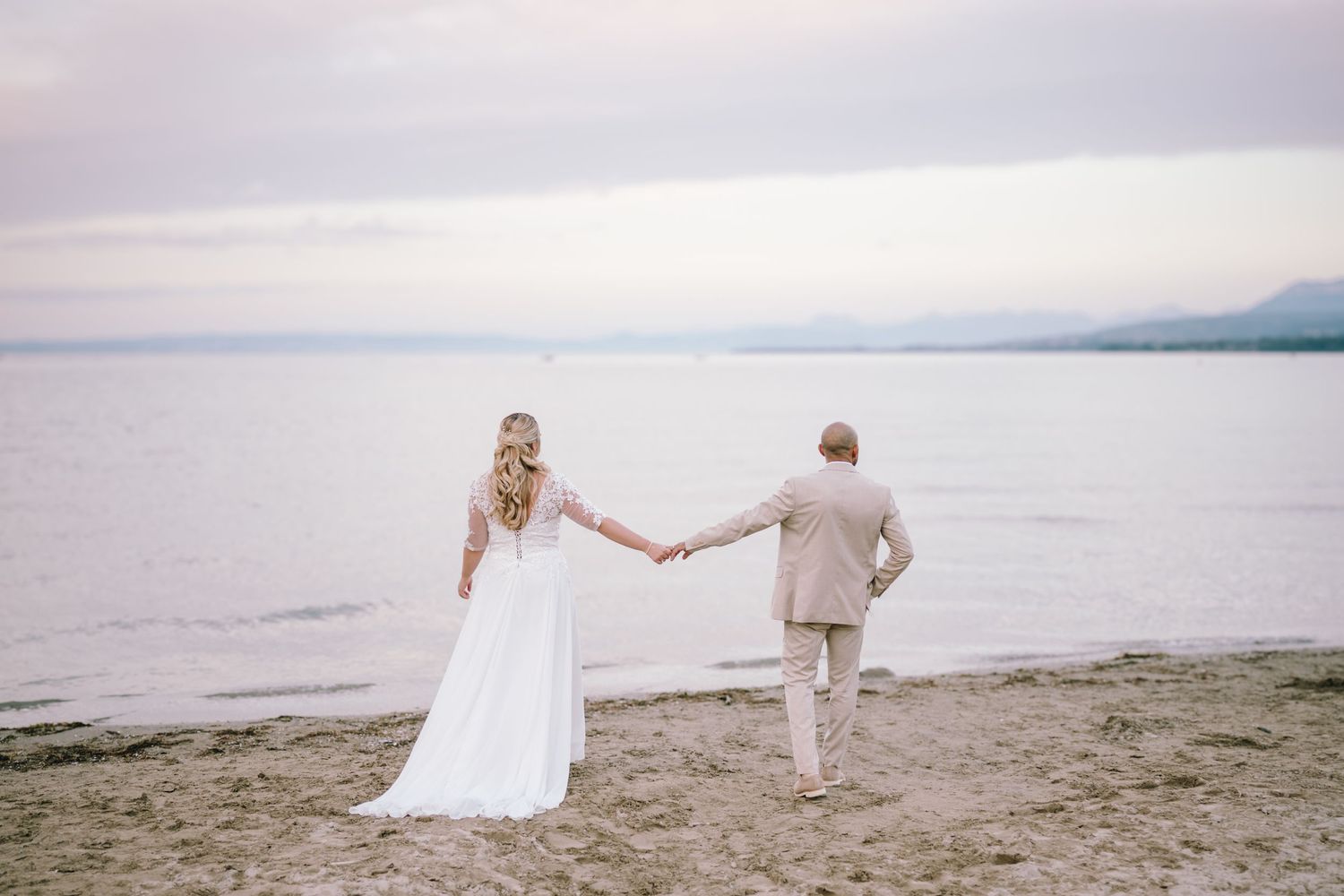 A just married couple with their wedding outfit walking towards the beach at lake Geneva in Switzerland during a beautiful sunset afternoon