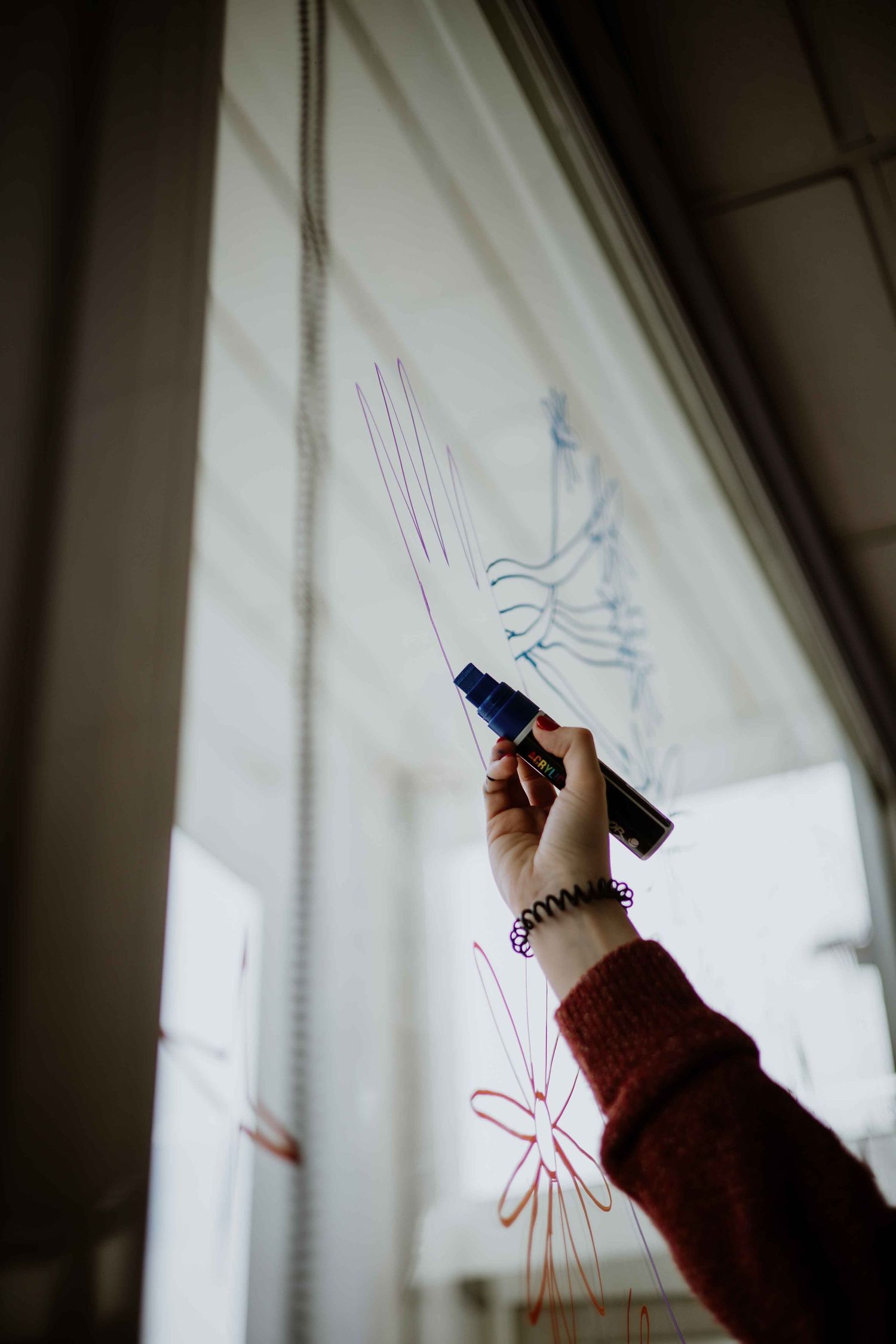 Hand in a burgundy sleeve drawing lines on a white surface with a marker.