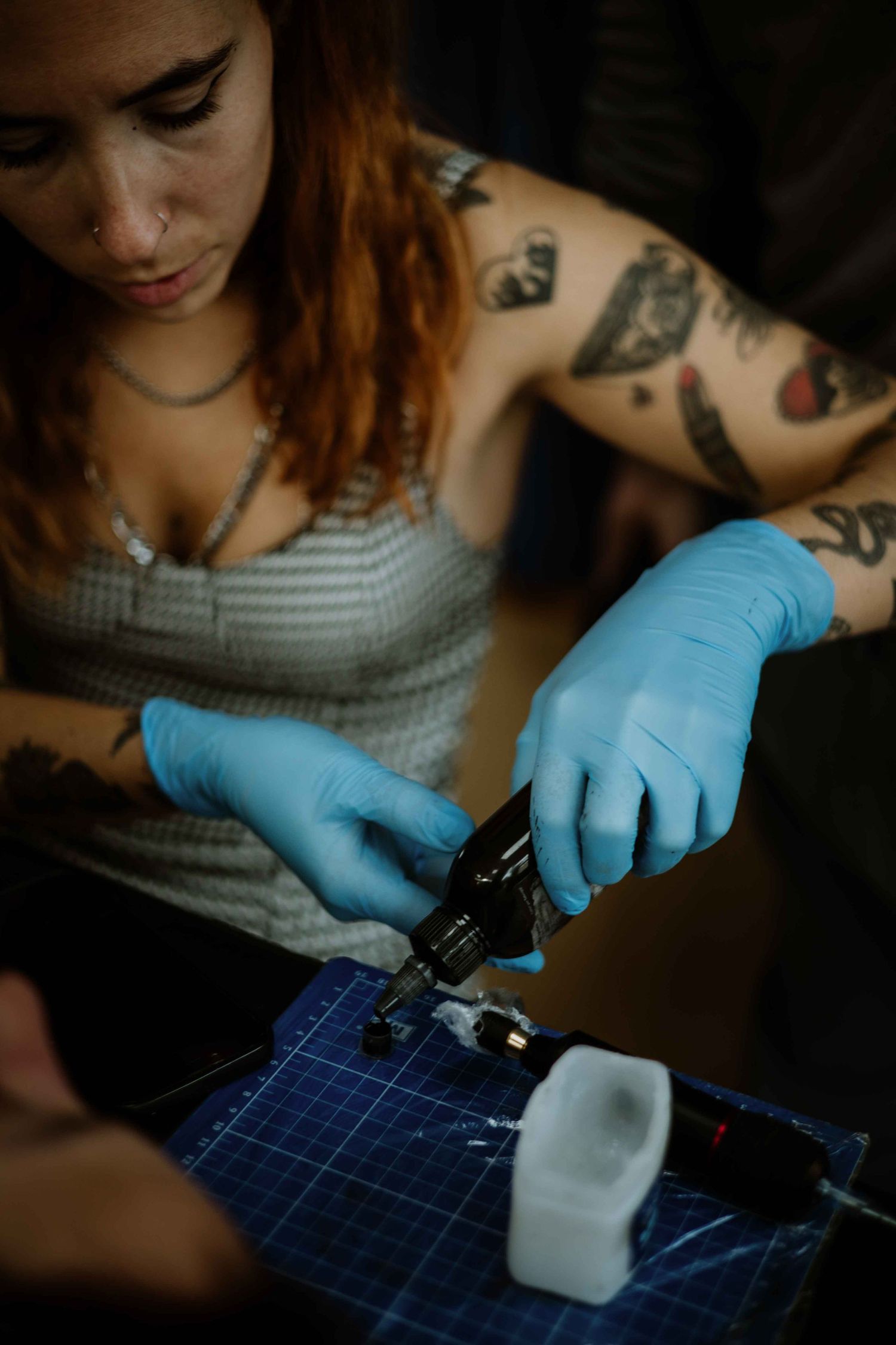 Person wearing blue gloves working with tools on a gridded surface.