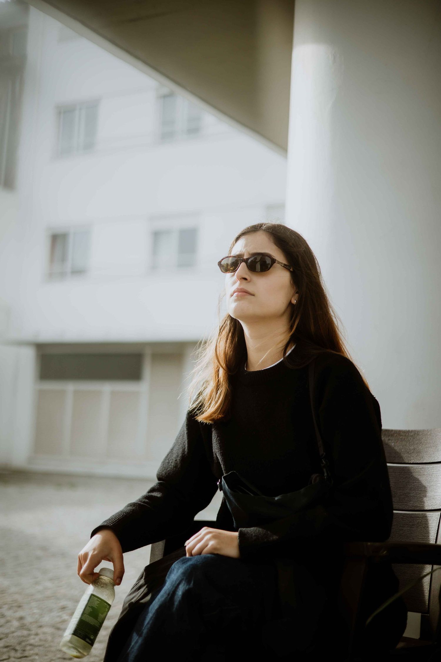 Person in black clothing and sunglasses sitting on a bench in foggy weather.