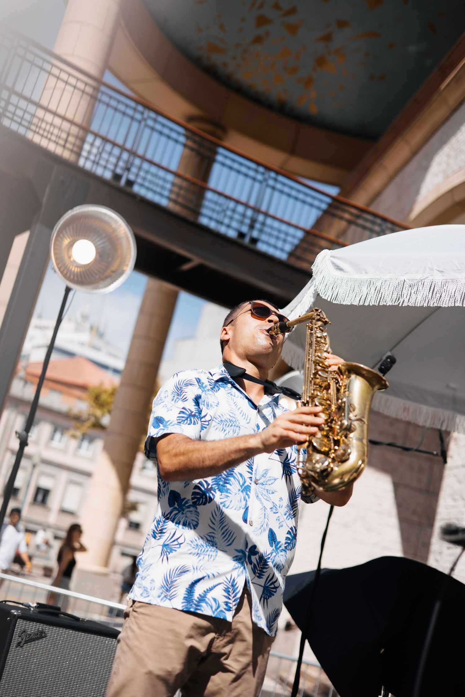 Registo urbano de um saxofonista a atuar ao ar livre, envolto em som, cor e movimento.