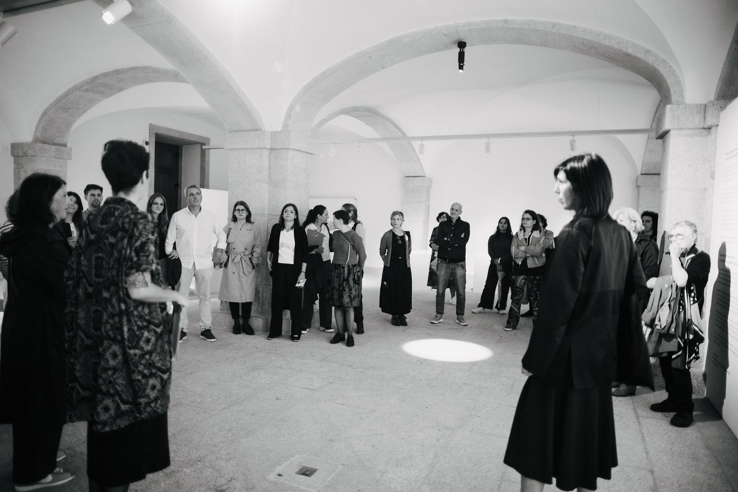 Black and white photograph of people gathered in an arched gallery space for an exhibition.