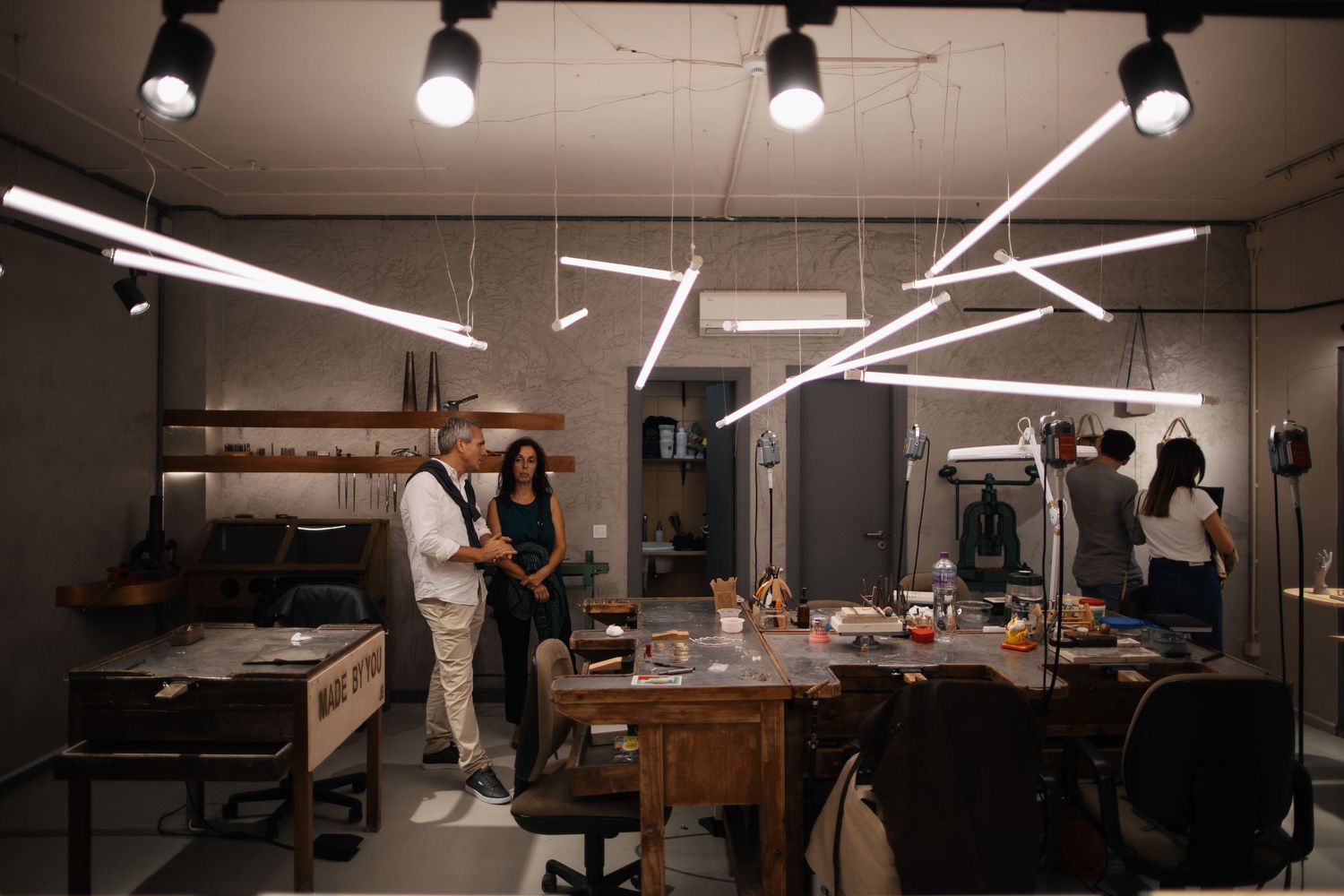 Modern workspace with geometric LED lighting fixtures and people gathering around wooden tables.