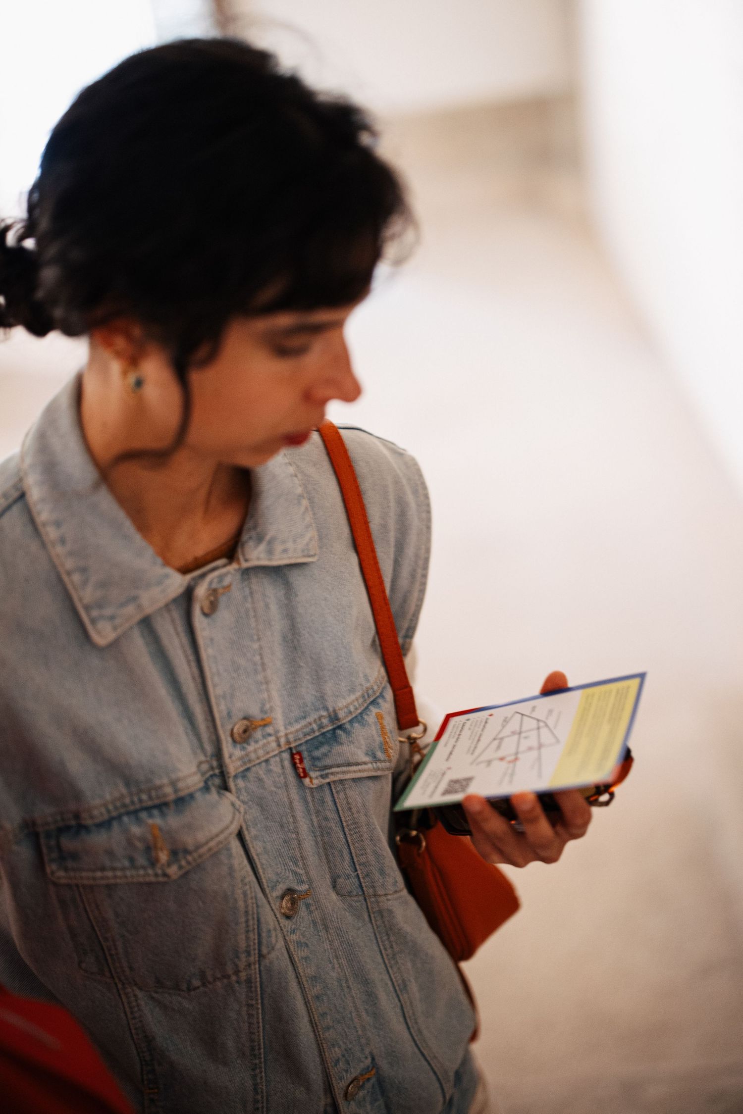 Person wearing denim jacket examines exhibition materials in art gallery.