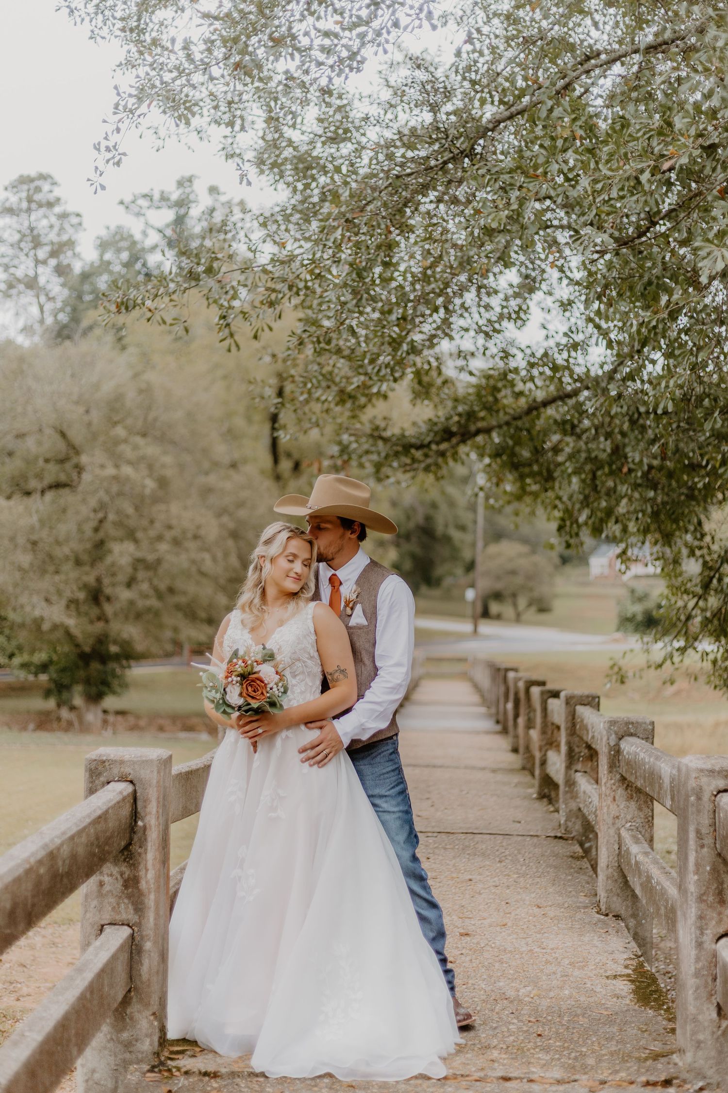 A romantic wedding photo captured through flowing white veil with orange floral bouquet details.