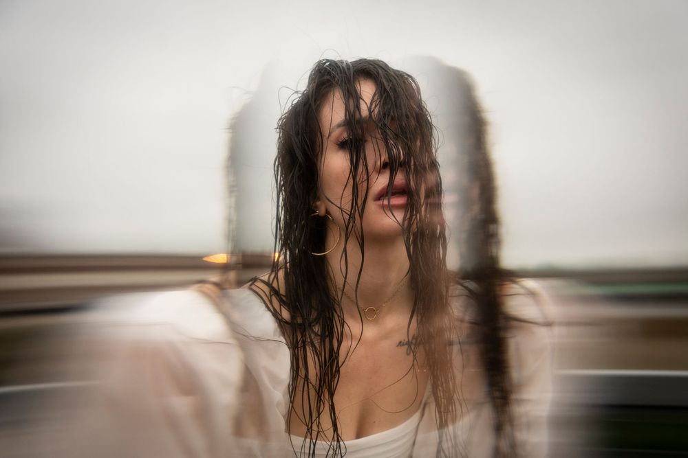 Artistic double exposure portrait showing motion blur of wet hair against soft neutral background in moody lighting.