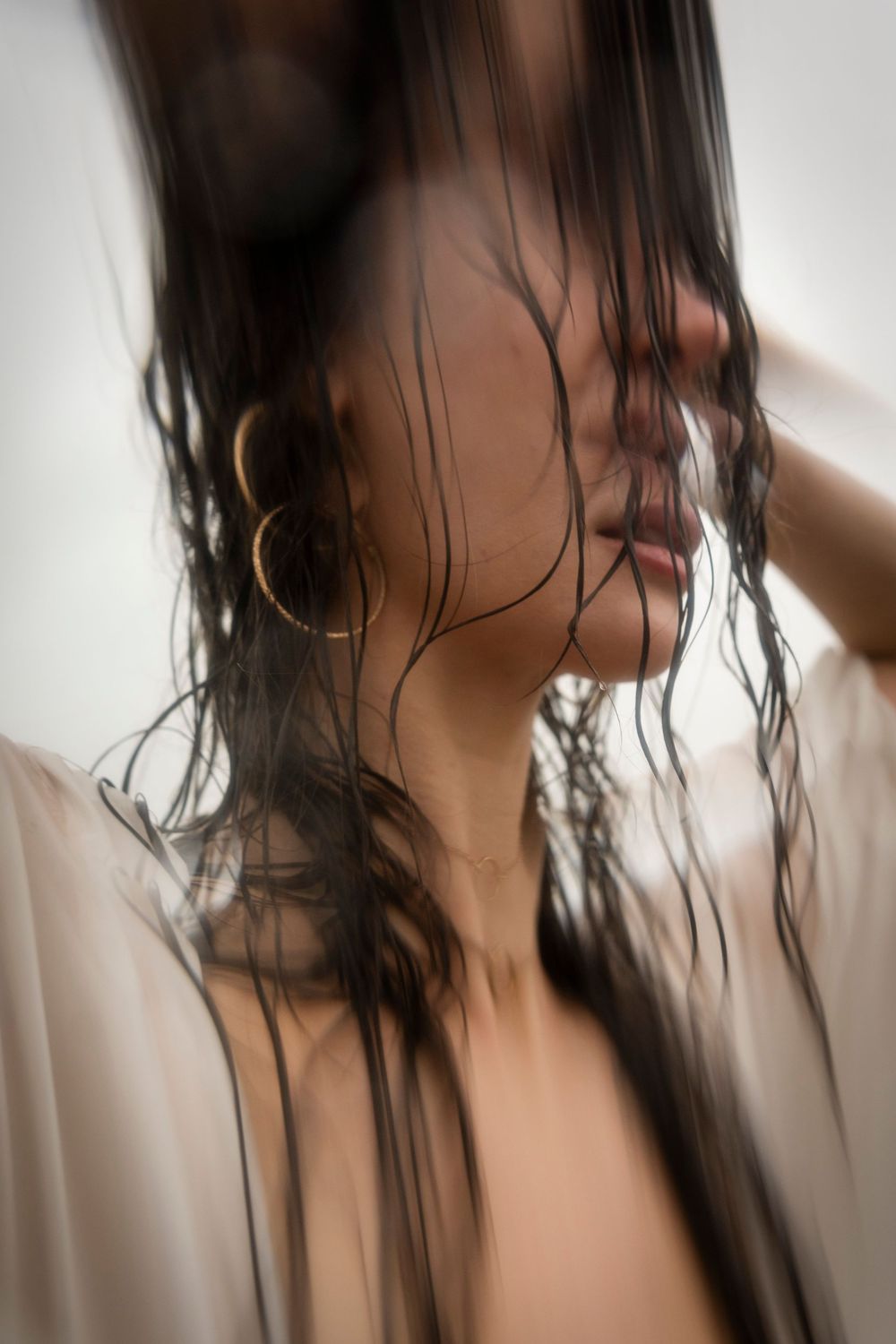Side profile portrait of wet dark hair against white background with gold hoop earring visible.