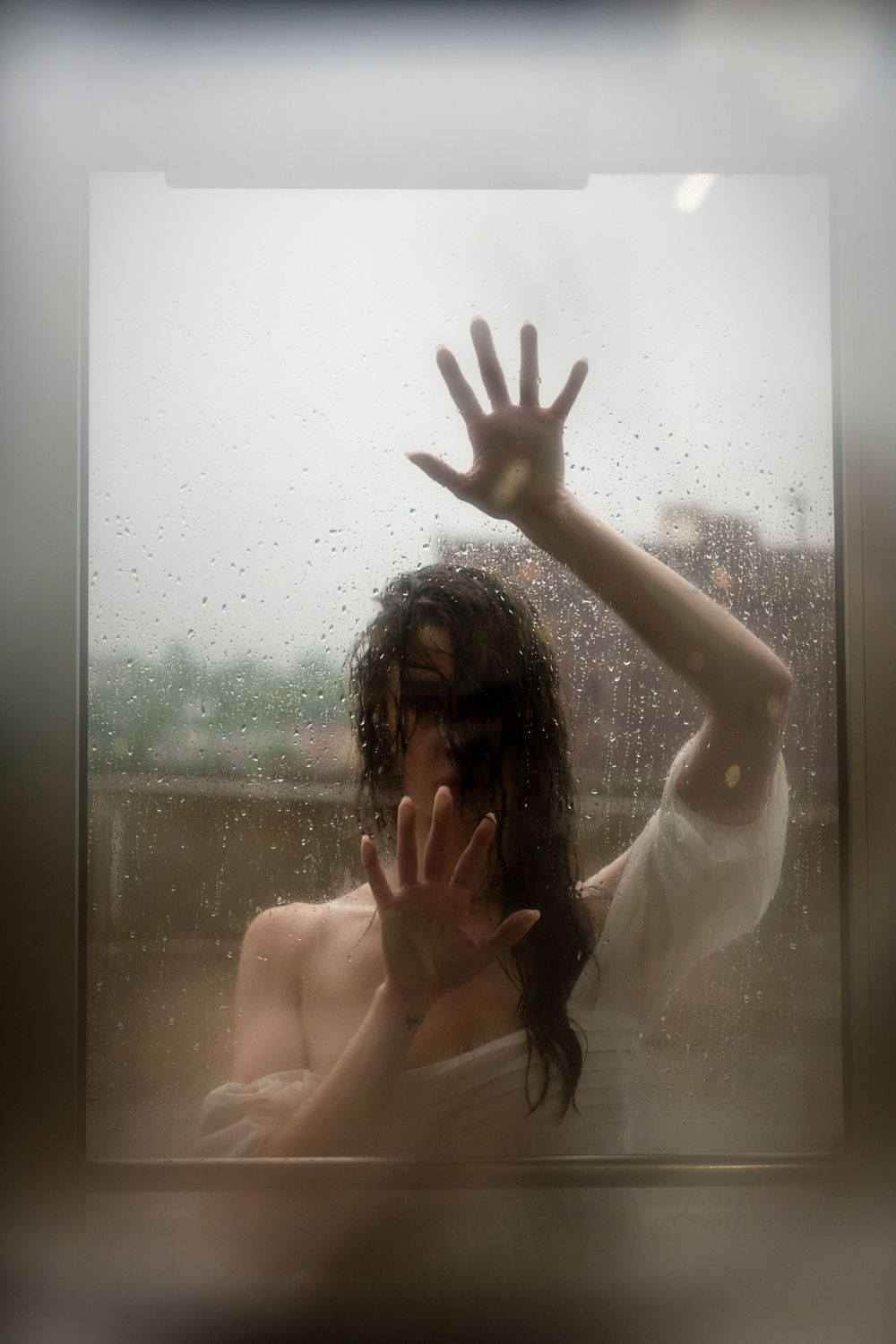 A silhouette behind frosted glass presses hands against the surface during a rainy day.