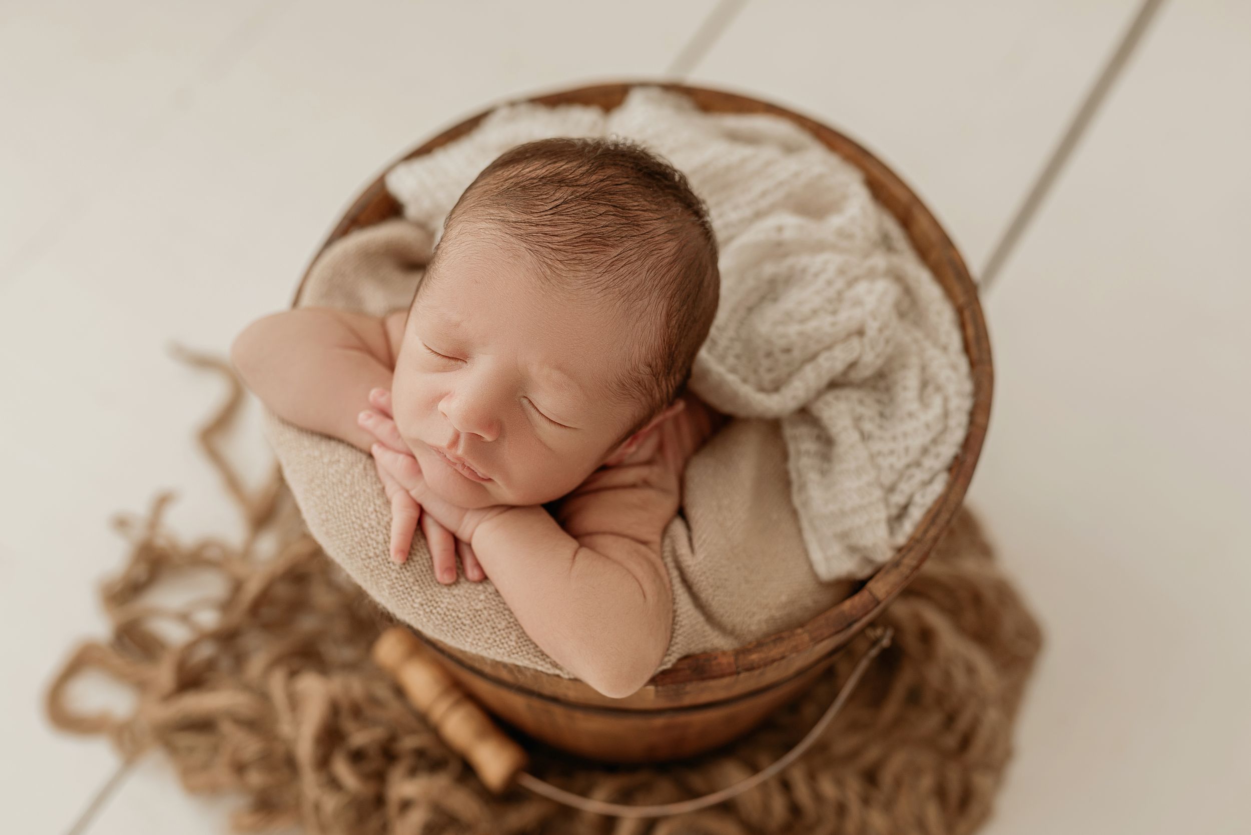 Sleeping newborn rests peacefully in wooden bowl lined with soft fabric.